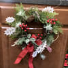 A small holiday wreath decorated with white leaves and red holly berries