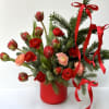 A festive holiday arrangement designed with lush evergreens, vibrant red tulips, ruby