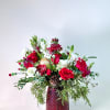 A festive holiday arrangement designed in a rich ruby-textured vase, overflowing with