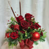Red roses, burgundy carnations sit amongst a mix of fragrant pines accrnted