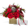 Red roses, winter greens, and a frosted pinecone designed in a gold