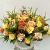 A charming autumn basket bursting with yellow, peach, and orange roses, accented