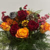 A warm, vibrant arrangement featuring rich red roses, amber-tipped orange roses, and
