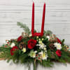 Long and low Christmas centerpiece made with 2 candles, pines, seasonal flowers