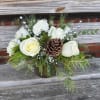 Evergreens, white roses, carnations, pinecones and touches of silver. Clear vase.