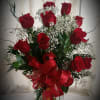 A dozen red roses arranged in a vase with fern and baby&#039;s