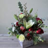 A rustic wood cube container filled with holiday greenery, white lilies, roses