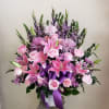 Pink and purple floral arrangement in a white container with a purple ribbon