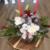A festive Christmas centerpiece featuring fresh evergreens, red candles, white carnations, daisies