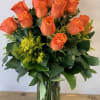 12 long stem orange roses with greens an fillers arranged in clear