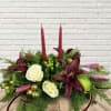 A traditional style centerpiece with two red taper candles, moody lilies, white