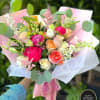 Hand-tied bouquet of pink peonies and mixed roses wrapped in pink paper with ribbon