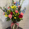 A tall, front facing linear arrangement of mixed colors. Lilies, roses, delphinium