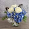 A clear glass vase with a cluster of blue hydrangeas, 3 white