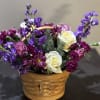 A charming woven basket overflowing with rich plum, violet, and ivory blooms.