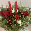 A timeless Candlelight No&euml;l centerpiece, handcrafted with fresh winter evergreens, rich red