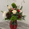 A huge red vase full of Christmas greens and Christmas themed flowers.