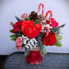 Fresh floral arrangement in rectangular glass vase with roses, carnations, holiday greens