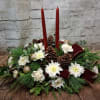 A traditional long and low Centerpiece featuring taper candles, assorted fragrant evergreens