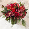A seasonal assortment of red flowers and holiday greens. Flowers subject to