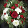 A beautiful arrangement including various winter greens, red roses, white cushions and