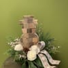 This cute wooden snowman is surrounded by winter foliage, white roses, pinecones