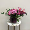 A dozen purple roses in a modern styled shorter vase with greenery