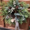 A holiday wreath with cream colored berries and ribbons, decorated with pinecones