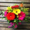 Assorted color gerbera daisies with greens and filler in clear gathering vase.