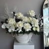 An elegant white arrangement featuring fresh roses, orchids, and a Christmas tree