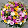 Vivid centerpiece contains mixed florals such as roses, ranunculus, lisianthus and others