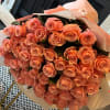 A modern hand-wrapped bouquet of 50 fresh cut roses in stunning coral