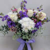 White roses, stocks, wax flower, daisies, and eucalyptus in a clear vase