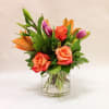 Mixed tulips and roses arranged with lilies in a small vase.