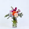 A vibrant, garden-inspired arrangement featuring lavendar lisianthus, orange ranunculus, fuchsia stock, soft