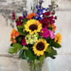 A tall, clear glass vase filled with bright, bold, and colorful flowers.