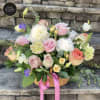 Basket arrangement of pink roses, white peonies, and pastel blooms with a pink ribbon