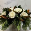 Arrangement filled with winter greens, magnolia, and white roses