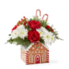 Filled with fresh winter pine and rich roses, this gingerbread house arrangement