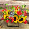 EXTRAVAGANT BLEND OF GLORIOSA LILY, SUNFLOWERS, AND BLUE DELPHINIUM ARRANGED IN SQUARE