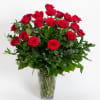 Two dozen long stem red roses arranged in a vase with decorative