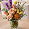 A lush, garden-style flower arrangement featuring roses, tulips, seasonal blooms, and decorative