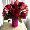 Alstromeria, roses, and carnations gathered in a small vase wrapped with hot