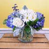 Blue and white flowers overflow in a clear glass cylinder inspired by