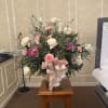 A urn vase with pink carnations, dark pink daisies and white roses.