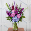 Pink, lavender and blue blossoms classically arranged in a clear vase, making