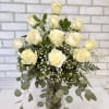 A dozen white roses arranged in a vase with filler and greenery.