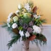 This arrangement features white roses, red blooms, lush evergreens, and festive accents
