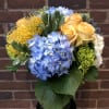 Butterscotch roses and pincushion protea float among blue and green hydrangea. Make
