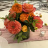 A bright beautiful arrangement made in citrus shades of zinnias, marigolds, roses
